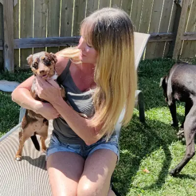 Profile photo of Elizabeth Taylor holding a small dog in a yard.